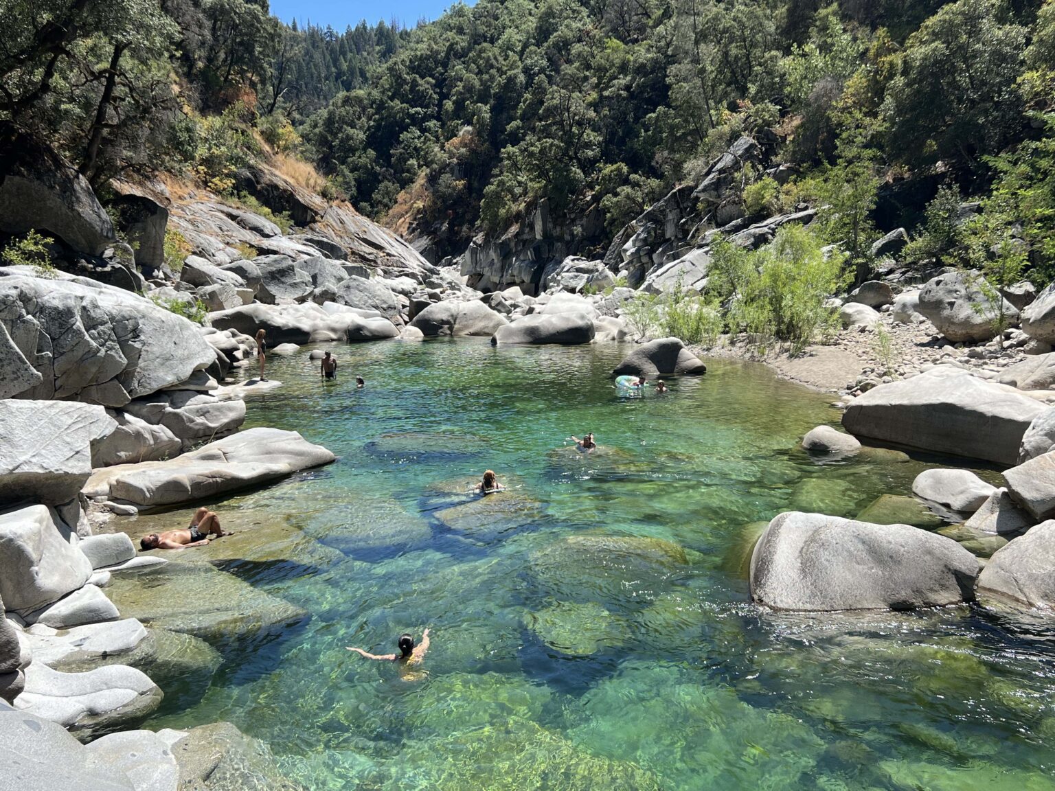 People swimming in the emerald-green Yuba River with granite boulders
